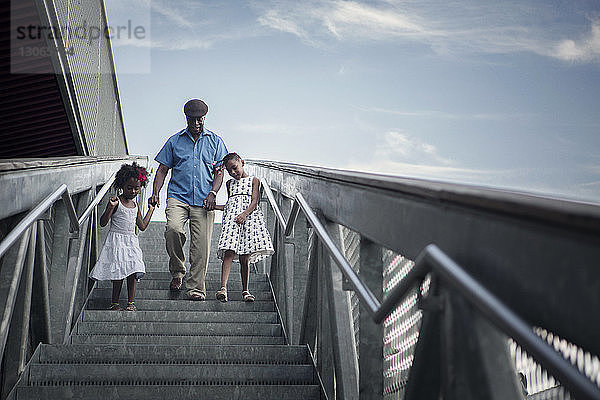 Großvater und Enkelkinder in voller Länge die Stufen gegen den Himmel hinuntergehen