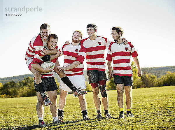 Porträt einer fröhlichen Rugby-Mannschaft auf dem Spielfeld vor klarem Himmel