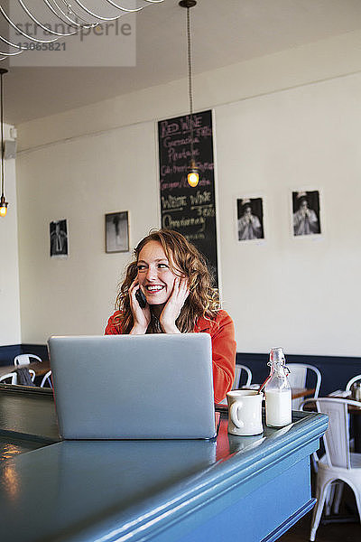 Lächelnde Frau spricht am Smartphone im Cafe