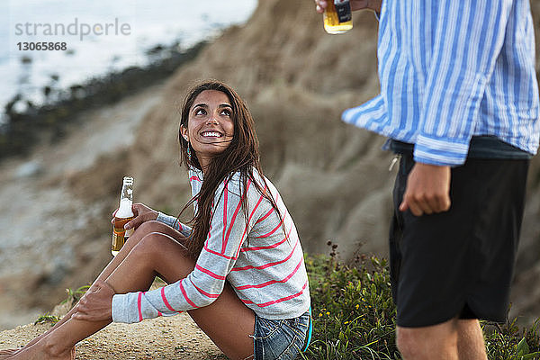 Frau mit Bierflasche schaut ihren Freund an  während sie auf dem Feld sitzt
