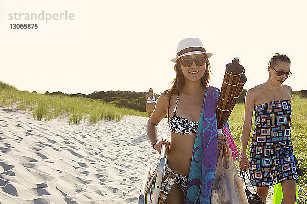 Porträt einer Frau  die Picknickdecken trägt  während sie mit einem Freund am Strand vor klarem Himmel spazieren geht