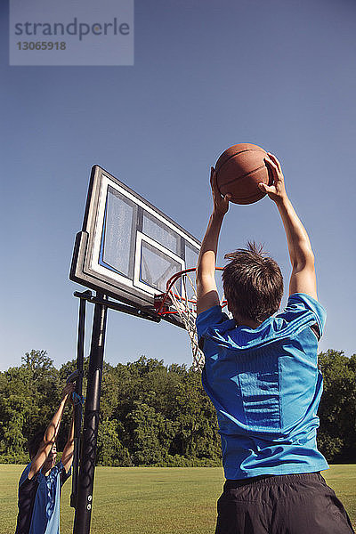 Jungen spielen Basketball an Bäumen gegen klaren Himmel