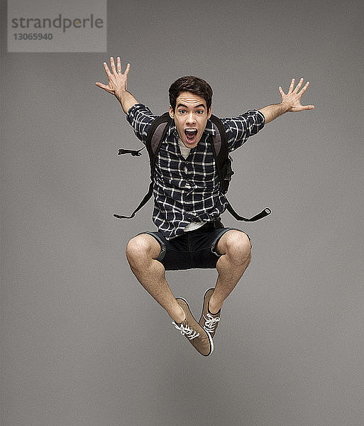Porträt eines fröhlichen Mannes mit springendem Rucksack vor grauem Hintergrund