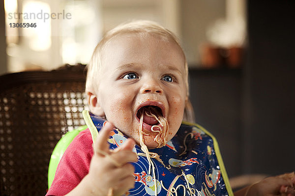 Kleiner Junge isst Nudeln  während er zu Hause auf einem Hochstuhl sitzt