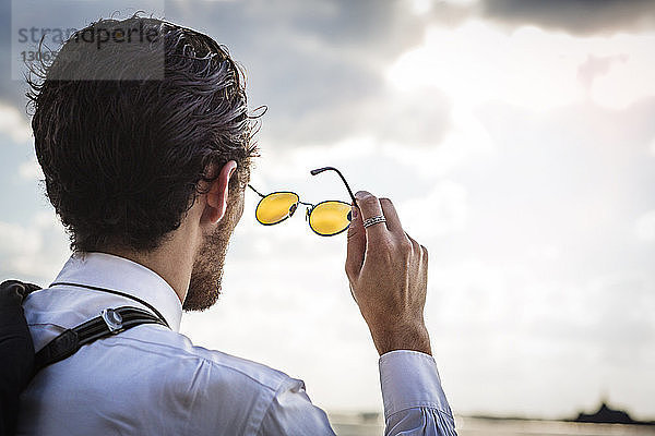 Rückansicht eines Geschäftsmannes mit Sonnenbrille  der gegen den Himmel schaut