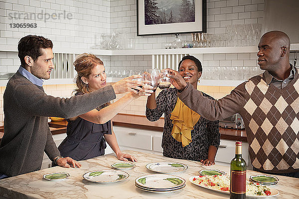 Glückliche Freunde stoßen am Tisch stehend auf Weingläser an