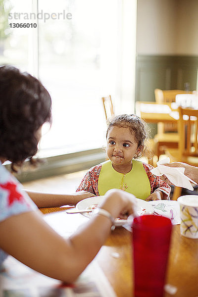 Mädchen sieht Mutter an  während sie im Restaurant am Tisch sitzt