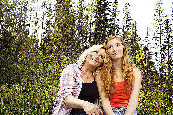 Nachdenklich lächelnde Mutter und Tochter sitzen an Bäumen im Wald