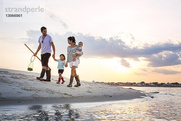 Eine Familie in voller Länge geht bei Sonnenuntergang am Meeresufer gegen den Himmel