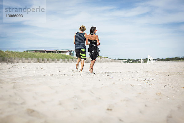 Rückansicht eines Paares  das auf Sand am Strand gegen den Himmel läuft