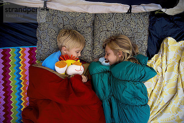 Draufsicht auf Geschwister mit Plüschtieren  die im Zelt schlafen