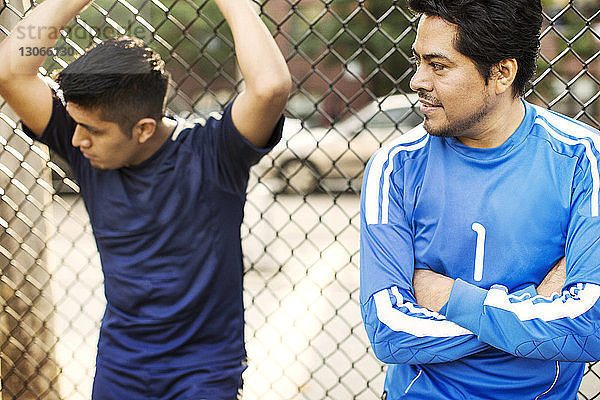 Männer schauen weg  während sie sich am Zaun am Fussballfeld anlehnen