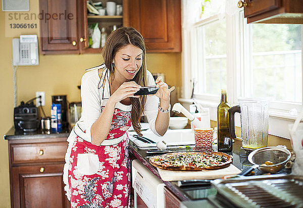 Frau fotografiert Pizza  während sie zu Hause in der Küche steht