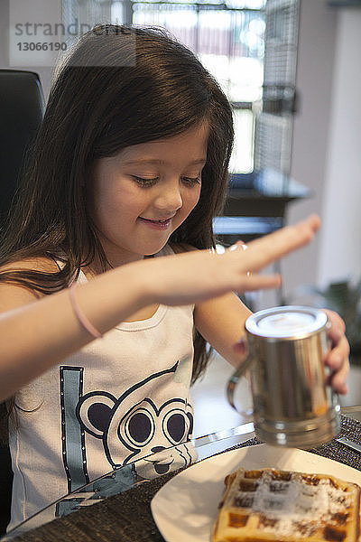 Mädchen bestreut Waffel mit Zucker  während sie zu Hause am Tisch sitzt