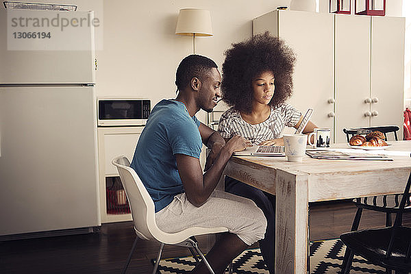 Ehepaar trinkt Kaffee  während es einen Laptop am Tisch in der Küche benutzt