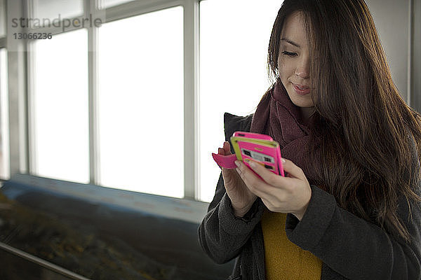 Frau benutzt Smartphone  während sie am Fenster steht