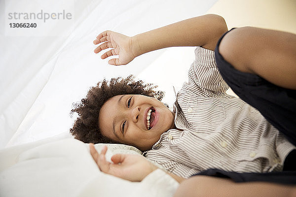 Verspielter Junge  der unter einer Decke auf dem Bett liegt