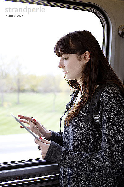Frau benutzt Tablet-Computer  während sie im Zug am Fenster steht