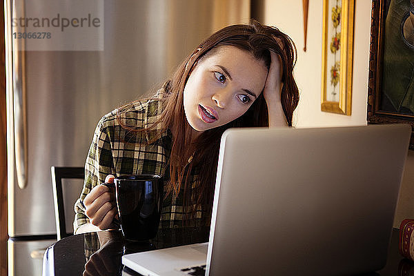 Kaffeetasse einer Frau  die zu Hause am Laptop sitzt