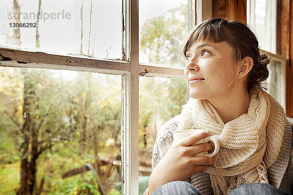 Frau schaut weg  während sie zu Hause am Fenster sitzt