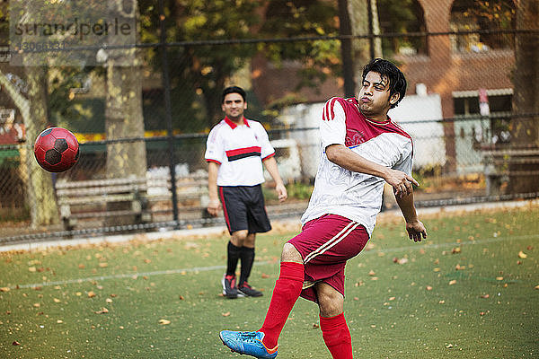 Fußballspieler kickt Ball  während ein Freund auf das Feld schaut