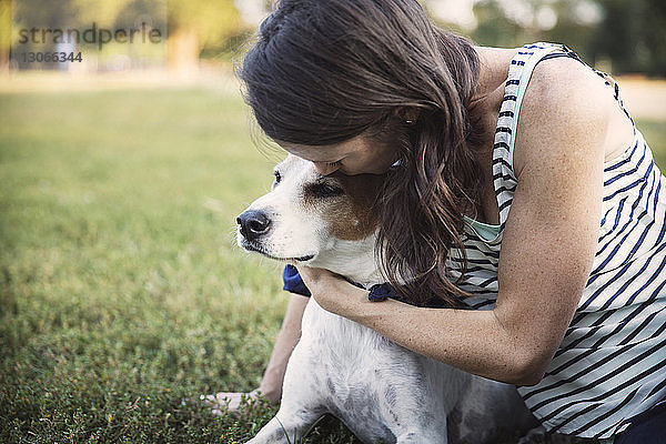 Liebende Frau küsst Hund  während sie sich auf Grasfeld im Park ausruht