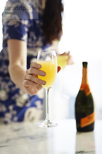 Mittelteil einer Frau  die ein Glas Saft hält  während sie zu Hause steht