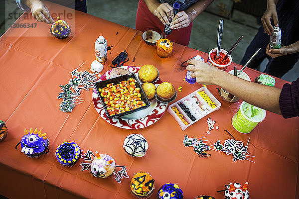 Mutter und Kinder dekorieren Muffins am Tisch während der Halloween-Party