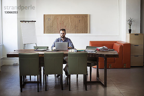 Mann benutzt Laptop-Computer  während er im Büro am Schreibtisch sitzt