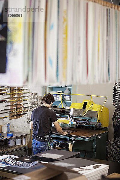 Rückansicht eines Mannes bei der Benutzung von Siebdruckmaschinen in der Werkstatt