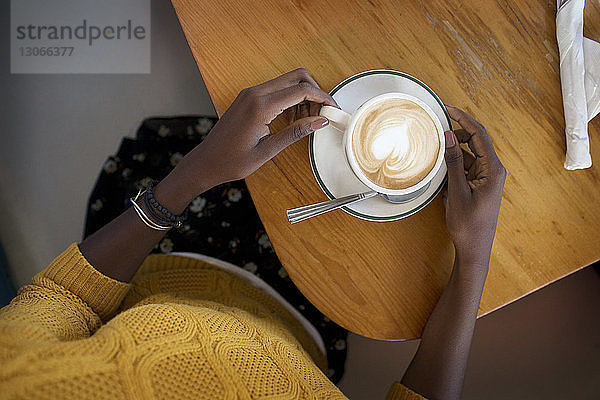 Ausschnitt einer Frau mit Cappuccino in der Hand  während sie im Café sitzt