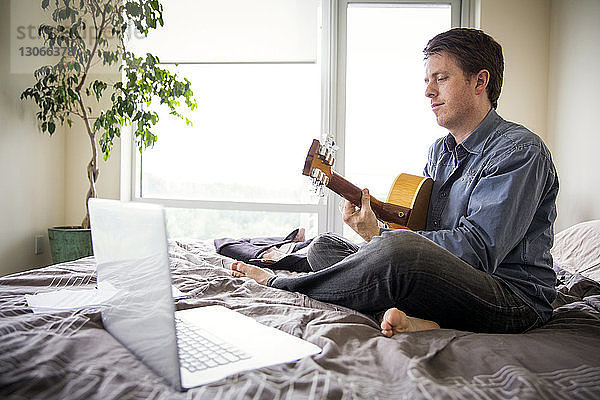 Mann benutzt Laptop-Computer  um zu Hause Gitarre zu lernen