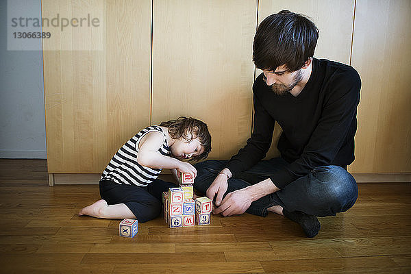 Vater sieht Tochter beim Spielen mit Spielzeugblöcken an  während er auf dem Boden sitzt