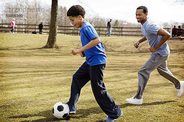 Seitenansicht von Vater und Sohn beim Fussballspielen auf dem Spielfeld im Park