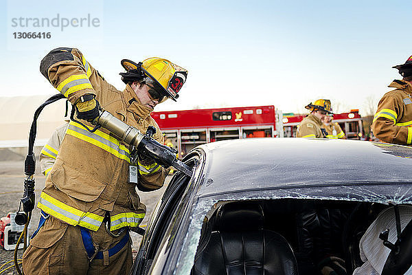 Feuerwehrmann schneidet Autofenster auf  während er gegen den klaren Himmel steht