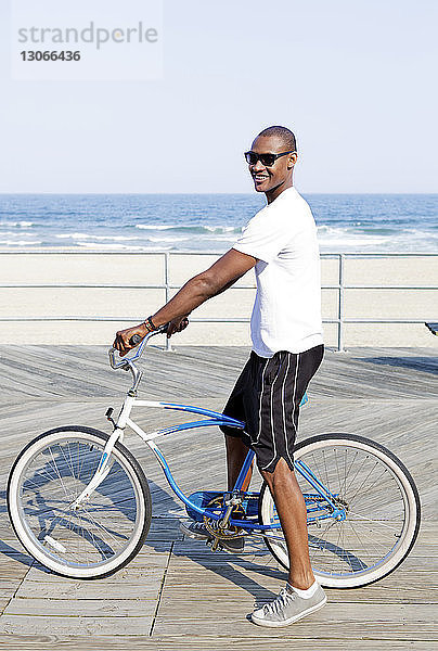 Mann mit Fahrrad auf Pier gegen Strand stehend