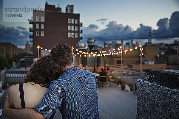 Rückansicht eines Paares  das sich bei Sonnenuntergang auf der Gebäudeterrasse entspannt