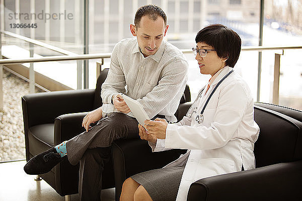 Ärzte schauen in den Tablet-Computer  während sie im Krankenhaus auf Stühlen sitzen