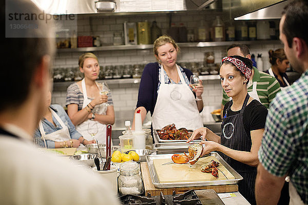 Köchin unterrichtet Studierende im Stehen an einer Großküche