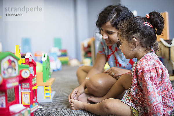 Mutter sitzt mit Mädchen zusammen  während sie zu Hause mit Spielzeug spielt