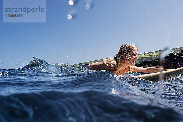 Frau surft im Meer bei klarem Himmel