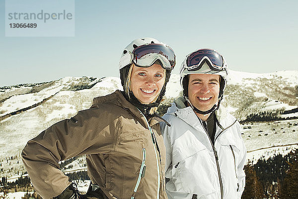 Porträt eines glücklichen Paares in Skikleidung  das vor schneebedecktem Berg steht