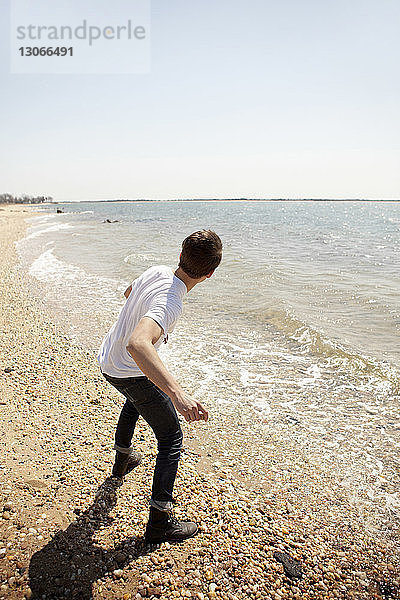 Rückansicht eines Mannes  der am Ufer stehend Steine ins Meer wirft