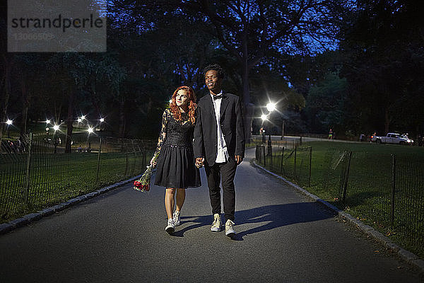 Glückliches Paar hält sich an den Händen und geht nachts auf einem Fußweg