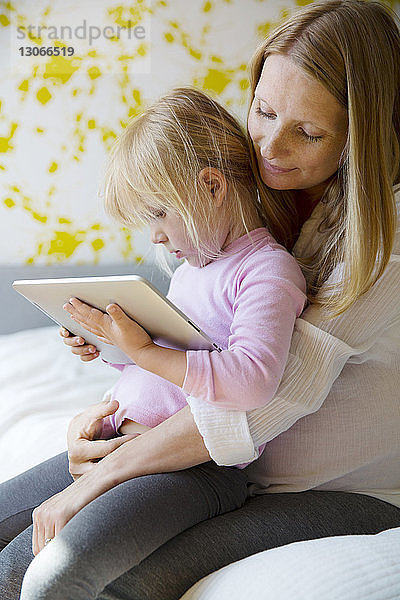 Mädchen benutzt Tablet-Computer  während sie mit der Mutter zu Hause im Bett sitzt