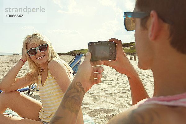 Mann fotografiert Frau  während er am Strand sitzt