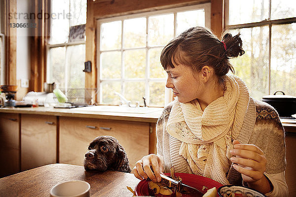 Frau sieht Hund an  während sie zu Hause Früchte bei Tisch schneidet