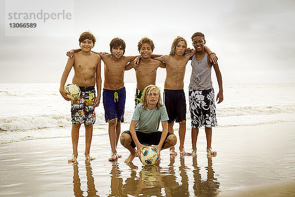 Porträt von Freunden mit Fussball am Strand am Ufer