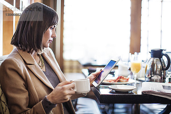 Frau benutzt Tablet-Computer  während sie im Restaurant am Tisch sitzt
