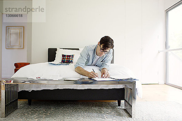 Mann arbeitet zu Hause im Bett an Dokumenten  während er im Bett liegt